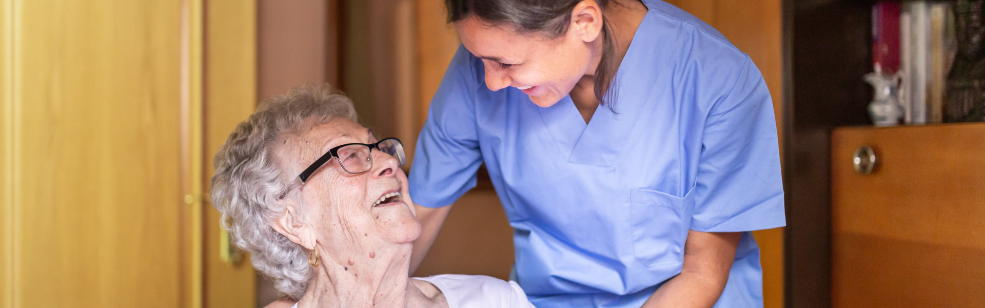 aide and senior woman with eyeglasses smiling at each other